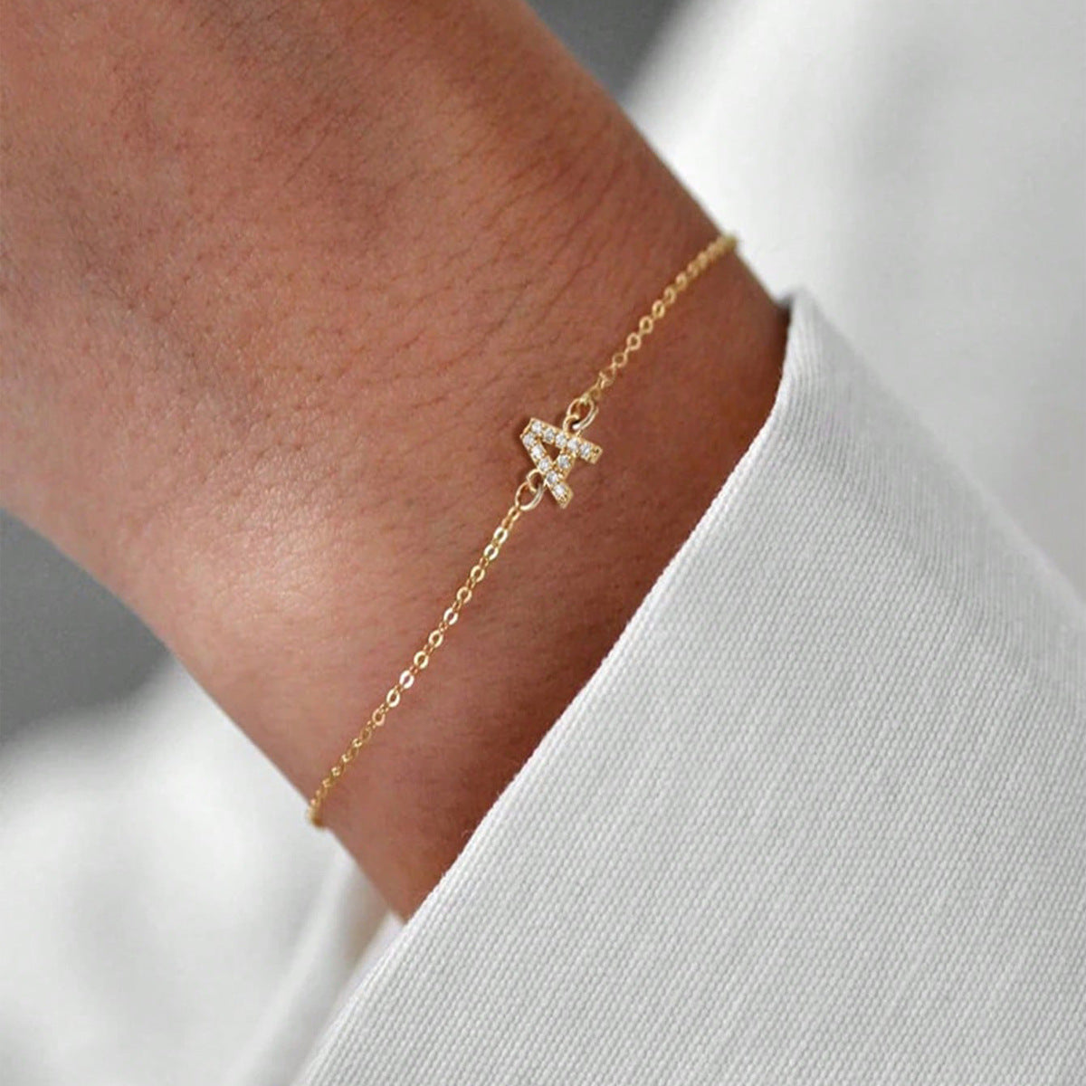 Gold crystal-set initial A bracelet on a fine chain worn at the wrist